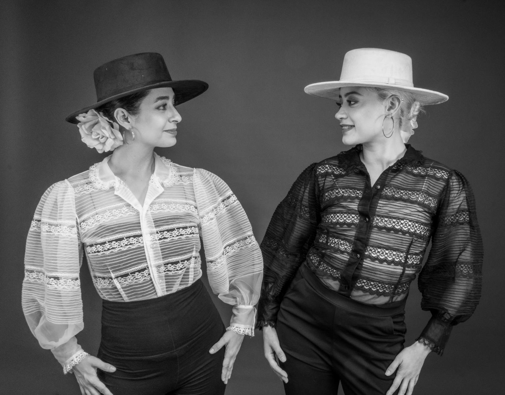 Dwie tancerki flamenco w eleganckich bluzkach i kapeluszach pozują
