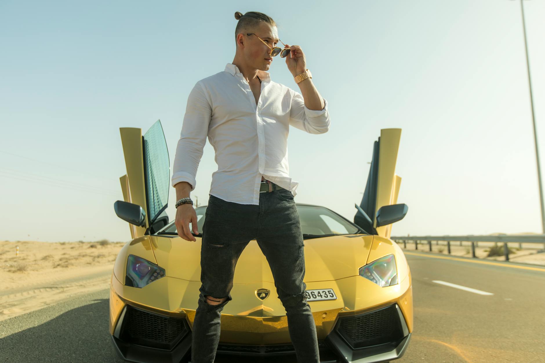 Mężczyzna pozujący przy żółtym sportowym aucie na pustynnym tle