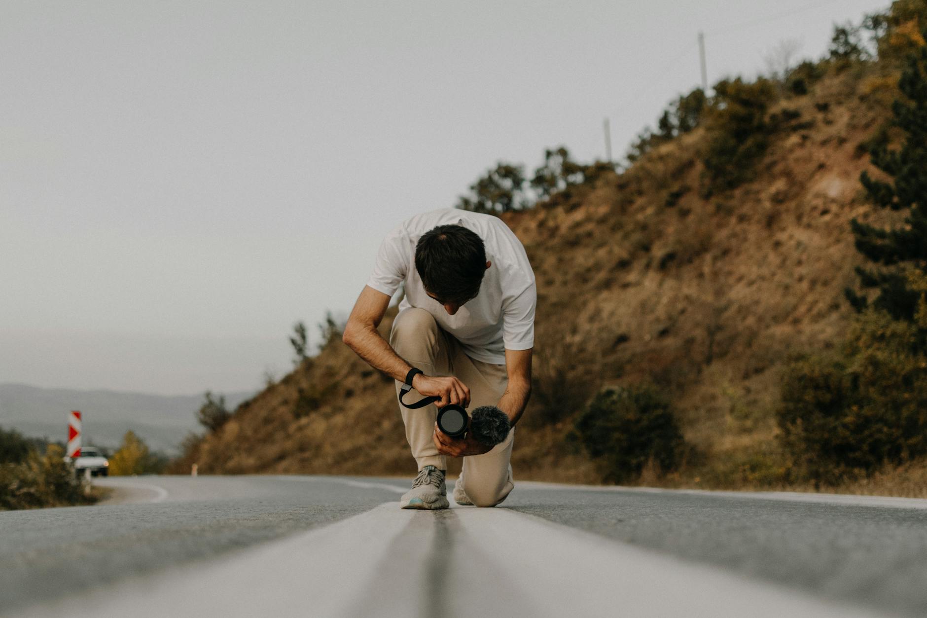 Fotograf klęczy na pustej drodze w górach podczas road tripu po USA