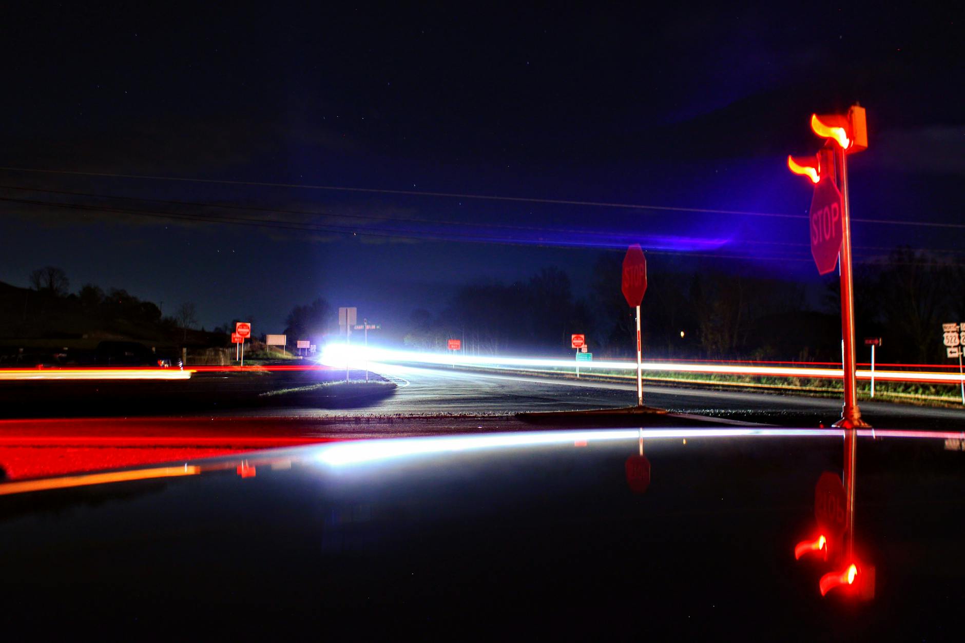 Nocne światła samochodów na wiejskim skrzyżowaniu ze znakami stop