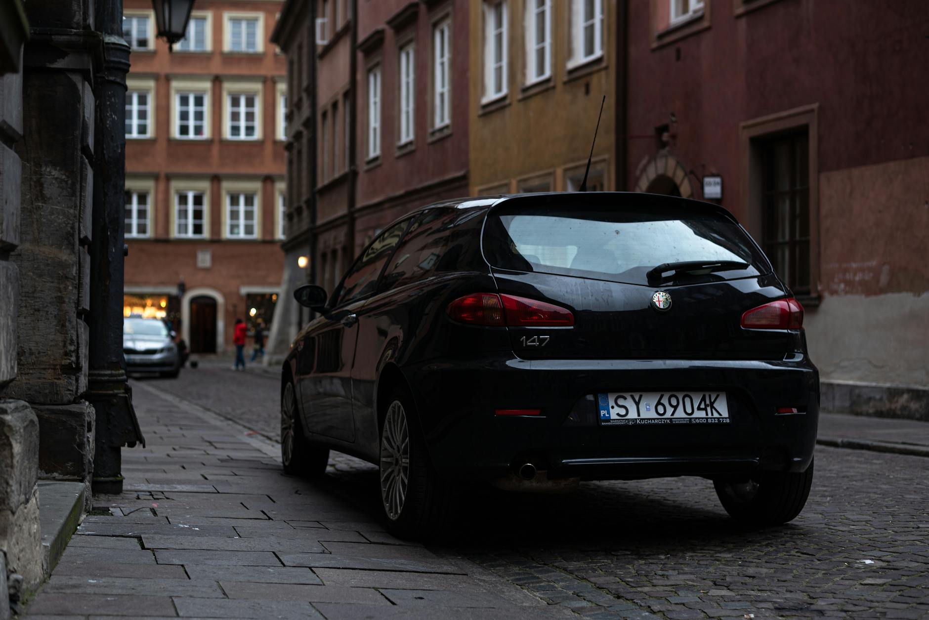 Czarny Alfa Romeo 147 zaparkowany przy starej ulicy w Warszawie